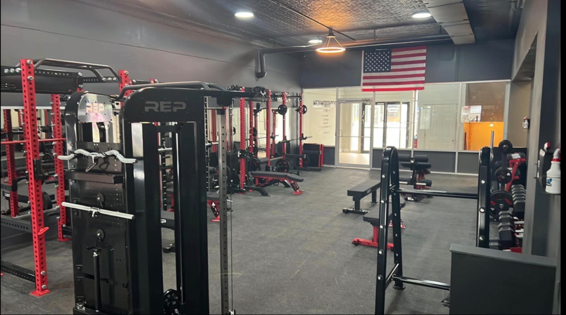 Gym floor with red REP power racks, benches and American flag