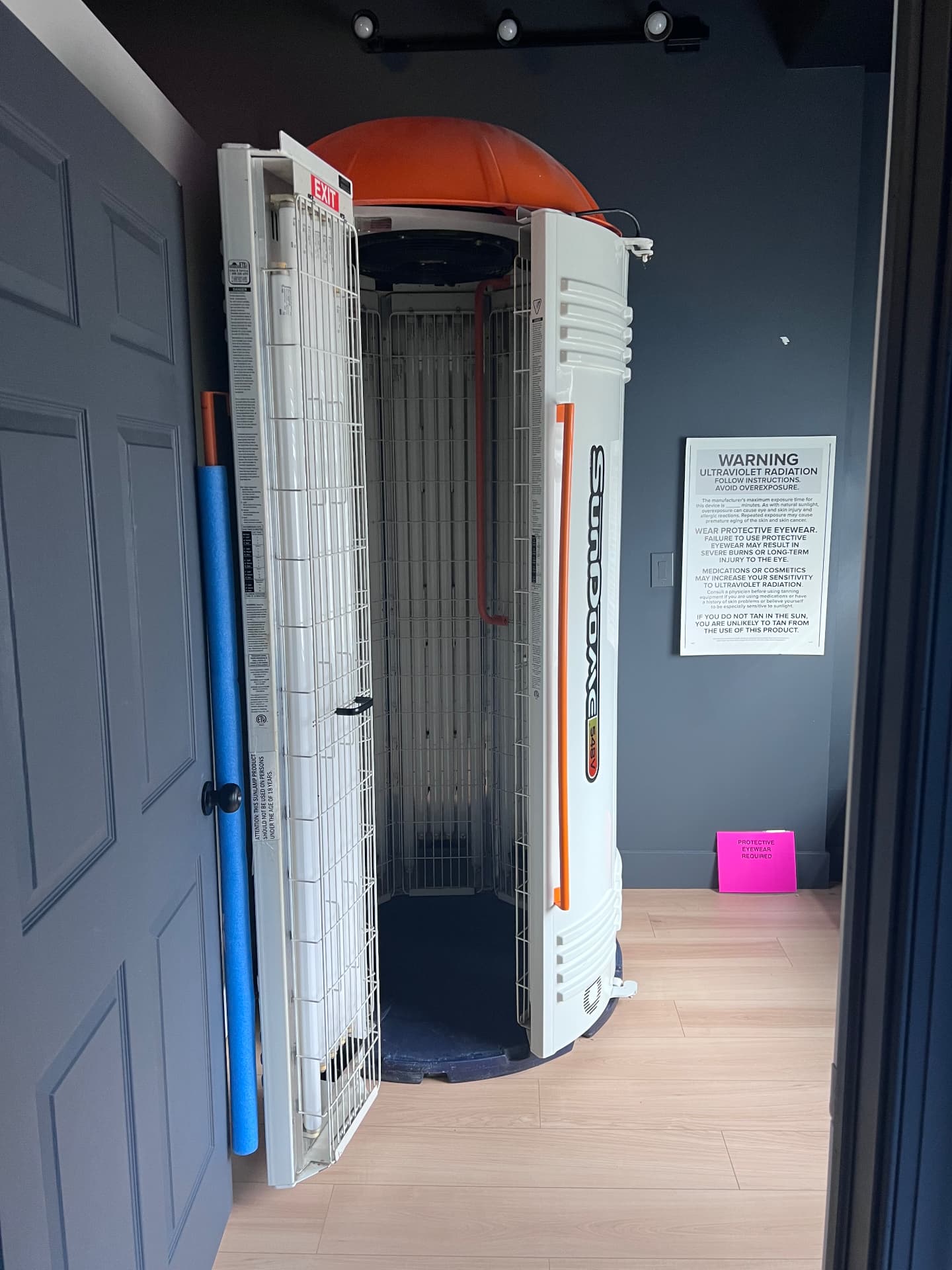 Open tanning bed in a private room with protective eyewear notice
